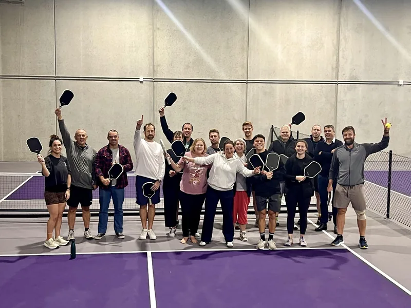 Group event participants holding pickleball paddles on the indoor courts